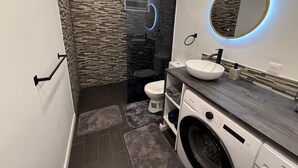 Une salle de bain moderne avec une douche à parois de verre, un miroir rond, un lavabo et un lave-linge.