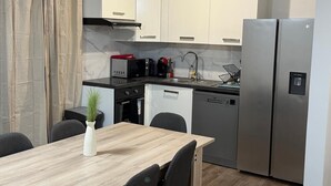 Une cuisine moderne avec des armoires blanches, des appareils en acier inoxydable et un coin repas comprenant une table et des chaises en bois.