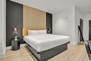 A modern bedroom with a large bed, a wooden headboard, and a black side table with a plant.