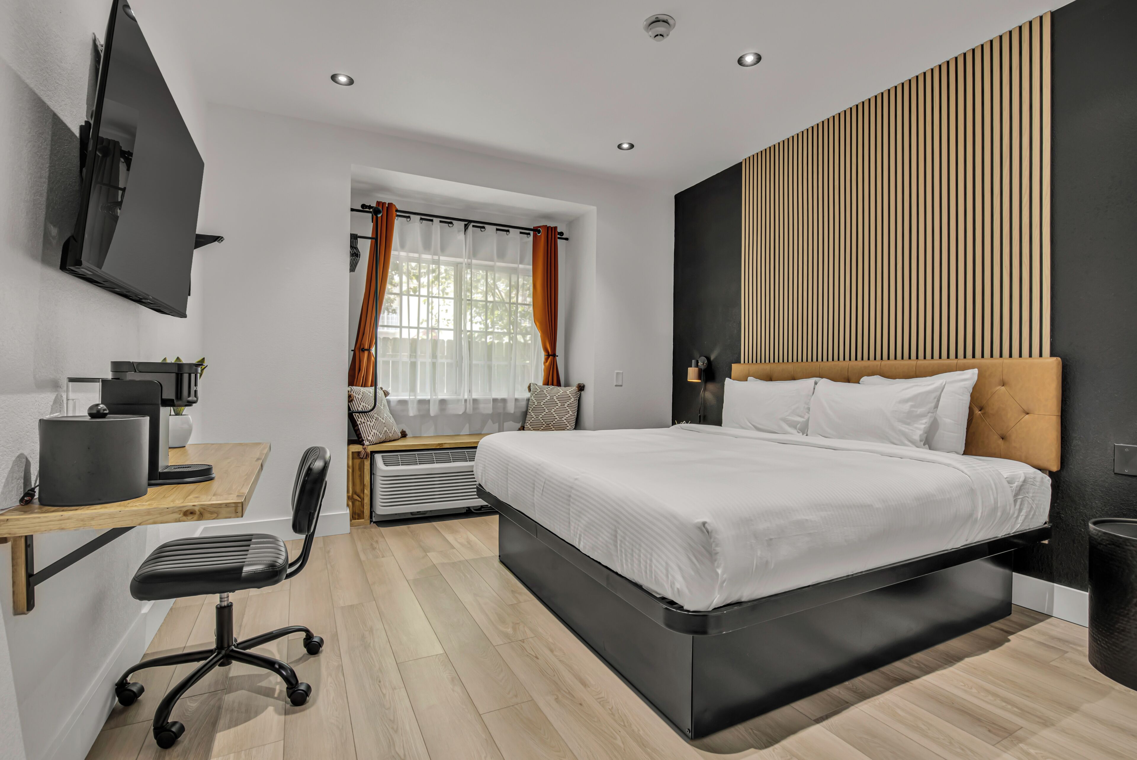 A modern bedroom with a large bed, a desk with a computer, and a TV mounted on the wall.