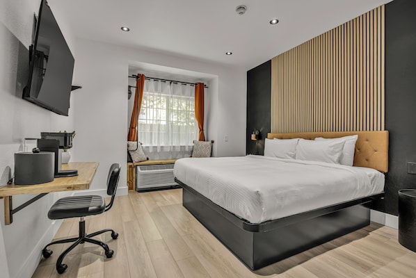 A modern bedroom with a large bed, a desk with a computer, and a TV mounted on the wall.