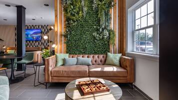 Uma sala de estar moderna com um sofá de couro marrom, uma mesa de centro redonda e uma parede decorada com plantas verdes.