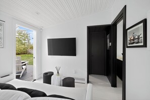 A modern hotel room with a large bed, a flat-screen TV mounted on the wall, a small table with a vase, and a door leading to a balcony. - Serene Designer Cottage Walking Distance to Town (Westhampton Beach)