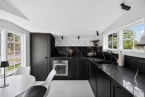 A modern kitchen with a black countertop, white chairs, and a large window. - Serene Designer Cottage Walking Distance to Town (Westhampton Beach)