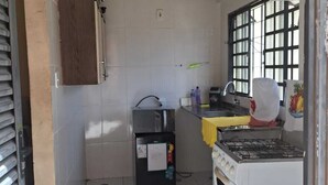 Eine kleine Küche mit einem Gasherd, einem Kühlschrank, einem Spülbecken und einem Fenster mit Gitterstäben.