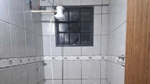 Eine kleine, geflieste Duschkabine mit Fenster, Brausekopf und Ablauforganisation.