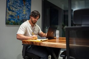 A person seated at a wooden table with a laptop and a notebook, writing. - Apartment Upper Level in Casco View (Panama City)
