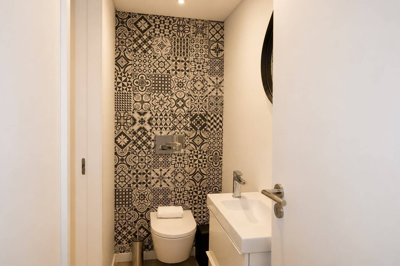 A small bathroom with a toilet, sink, and a wall with patterned tiles.
