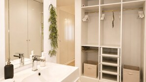 A modern bathroom with a large mirror, white sink, and a white walk-in closet with shelves and hanging space. - Lovely & Comfy I - Checkinhome (Monte Estoril)