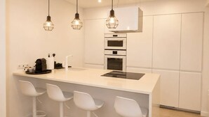 A modern kitchen with a central island, bar stools, a built-in oven, and pendant lighting. - Lovely & Comfy I - Checkinhome (Monte Estoril)