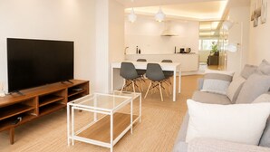 Una sala de estar moderna con un televisor de pantalla plana, una mesa de centro de vidrio, un sofá y un comedor con sillas y una mesa.