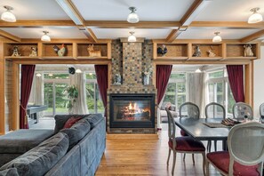 Una sala de estar con chimenea, vigas de madera y una zona de comedor con sillas y una mesa.
