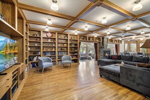 A spacious living room with wooden floors, built-in bookshelves, a fireplace, and a large TV. - Gorgeous Private Lakefront Estate w/Hot Tub, Kayaks & Stunning Views (Forestburgh)