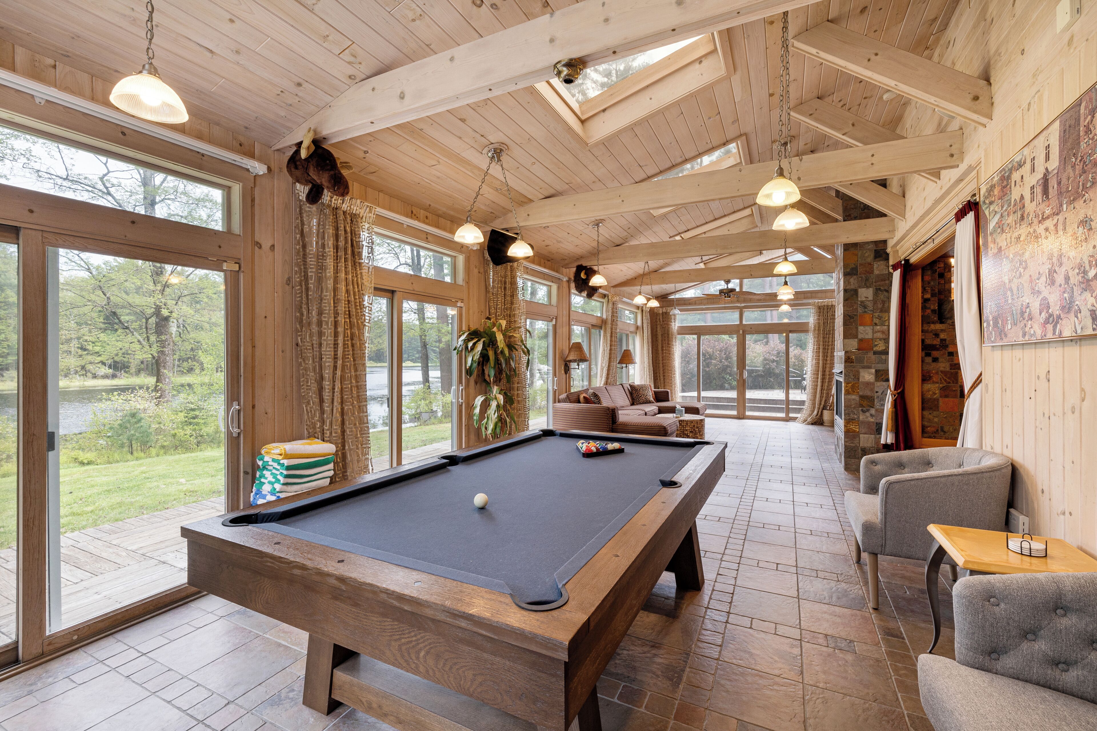 A pool table in a room with large windows, a sofa, and a chair.