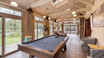 A pool table in a room with large windows, a sofa, and a chair.