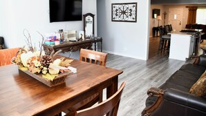 Un comedor con una mesa de madera, sillas, un centro de mesa decorativo, un televisor de pantalla plana, un reloj y una obra de arte enmarcada en la pared.