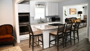 Una cocina moderna con armarios blancos, una isla central con taburetes de bar, horno integrado y microondas.