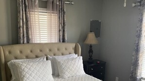 Una cama bien hecha con un edredón blanco acolchado, un cabecero y una mesita de noche con una lámpara.