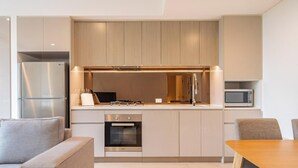 A modern kitchen with built-in appliances, a dining area with a table and chairs, and a sofa. - KozyGuru | Roseville | Modern Leafy Retreat (Roseville)