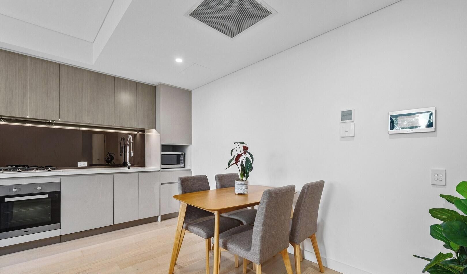 A modern kitchen with built-in appliances, a dining table with chairs, and a potted plant.