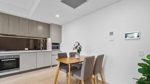 A modern kitchen with built-in appliances, a dining table with chairs, and a potted plant. - KozyGuru | Roseville | Modern Leafy Retreat (Roseville)
