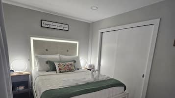 Un dormitorio con cama, mesitas de noche, un banco, una puerta y una lámpara en el techo.