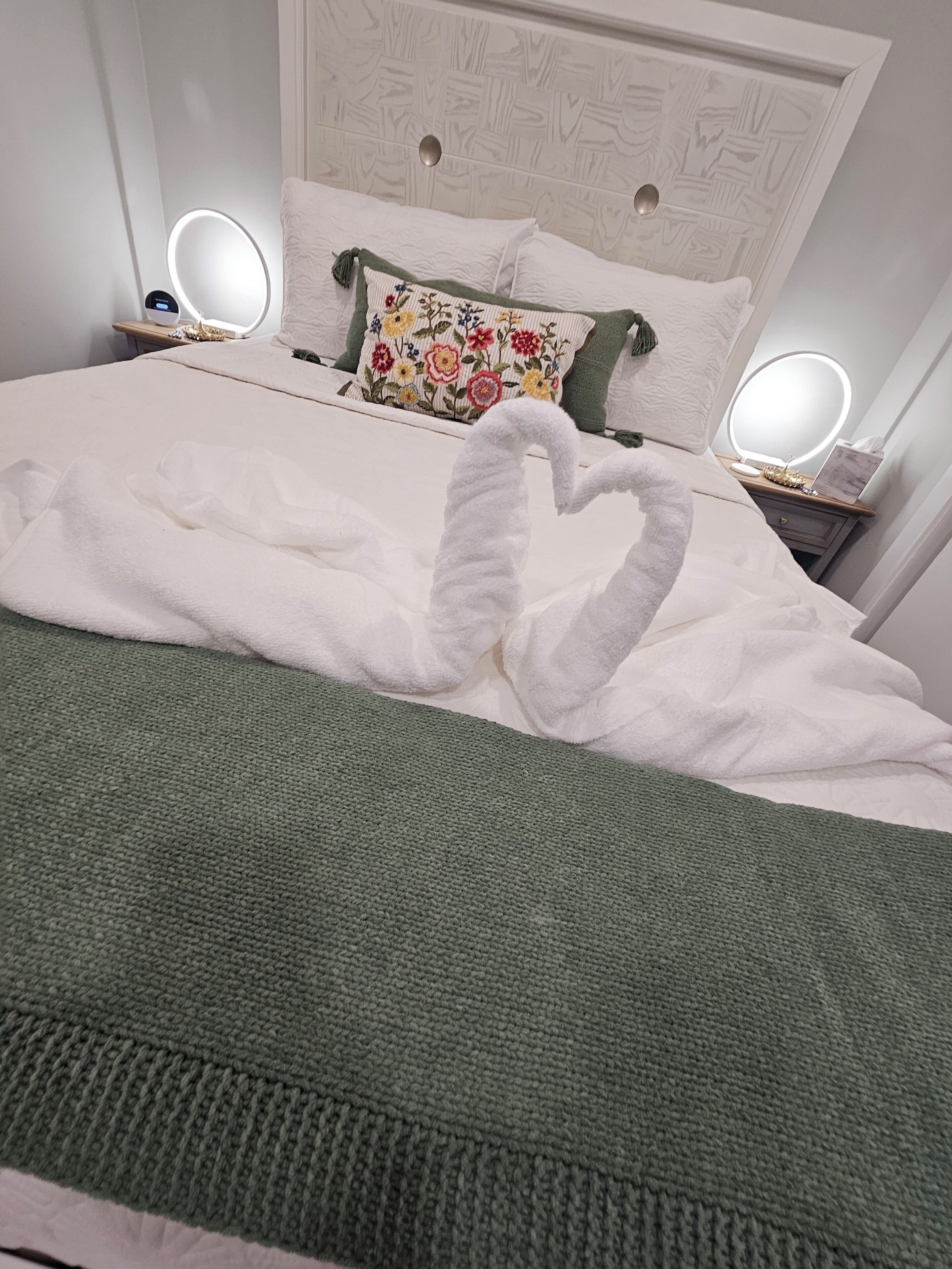 A neatly made bed with a green blanket and a swan-shaped towel arrangement.