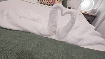 A neatly made bed with a green blanket and a swan-shaped towel arrangement.