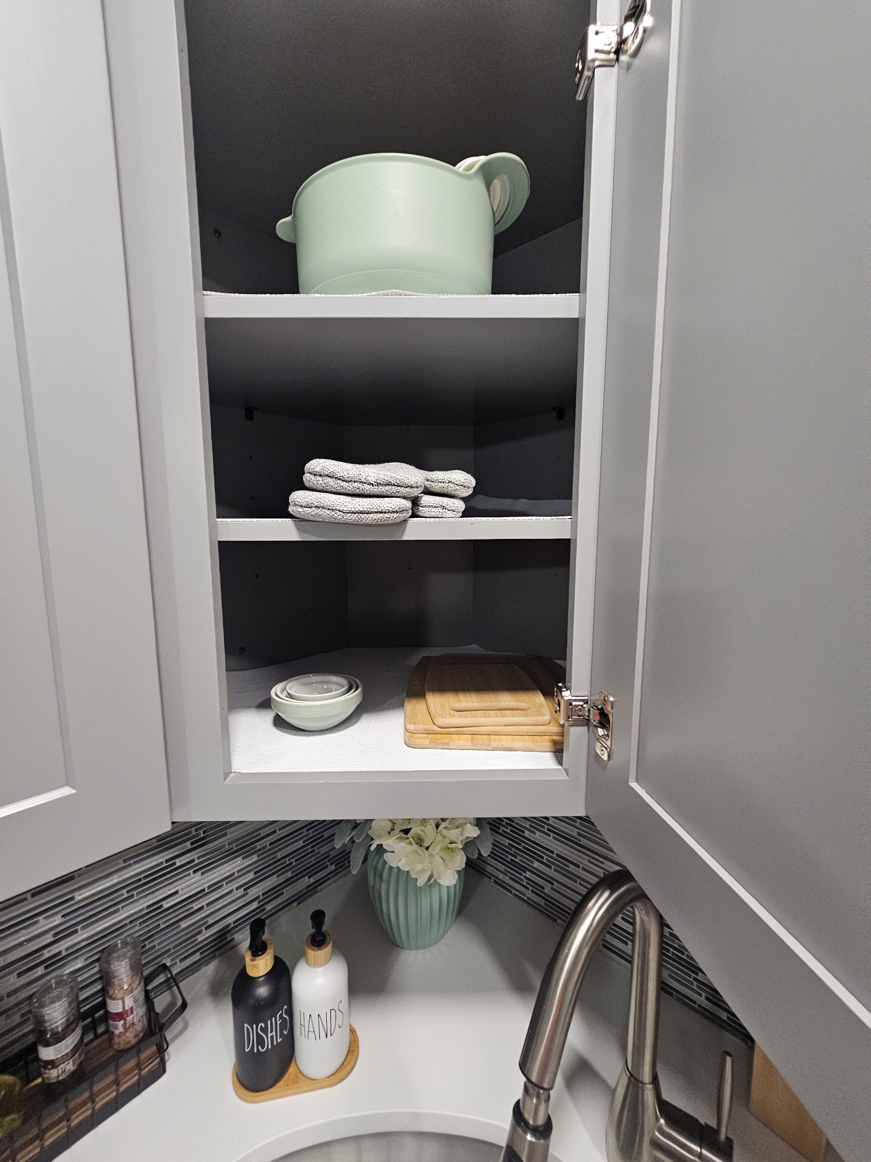 Una cocina con un lavamanos, una tabla de cortar, un bol y una botella de detergente.