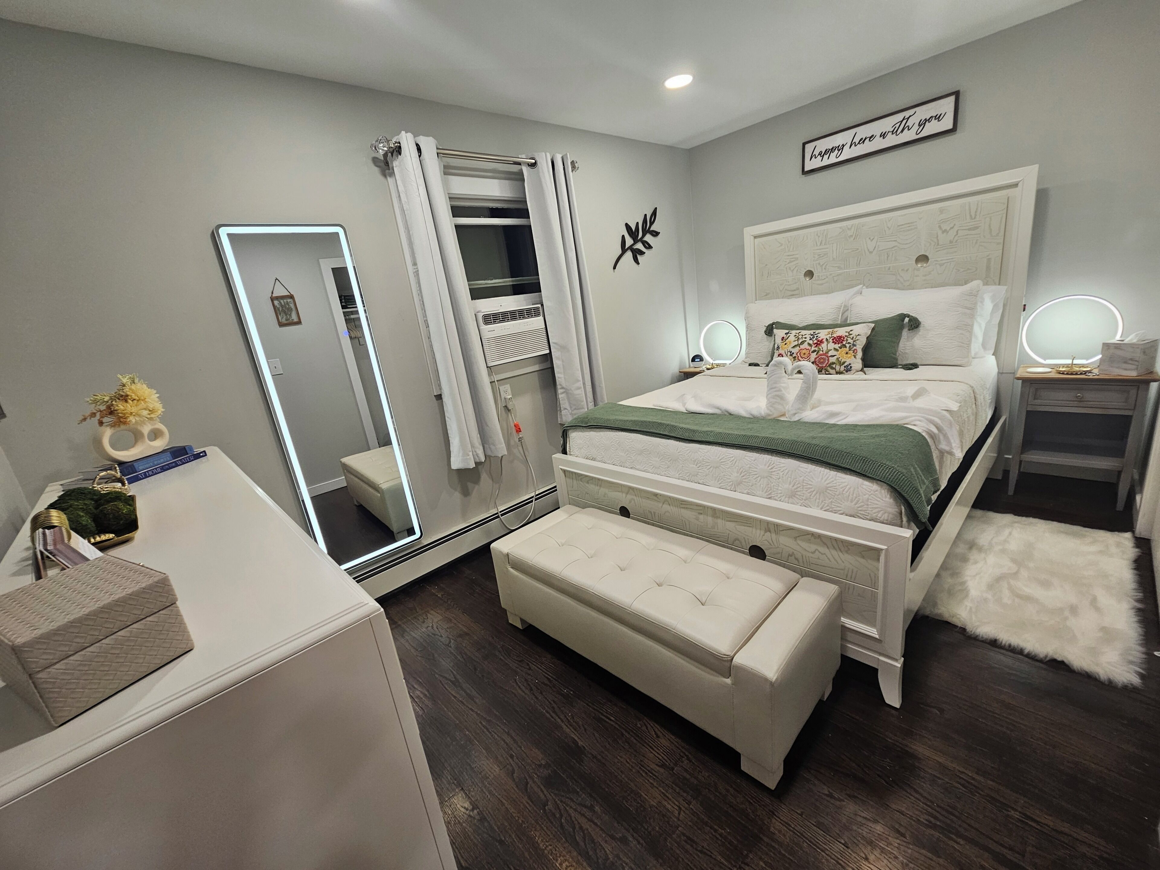 Une chambre à coucher comprenant un lit, des tables de chevet, un miroir, une coiffeuse, un banc et une armoire.