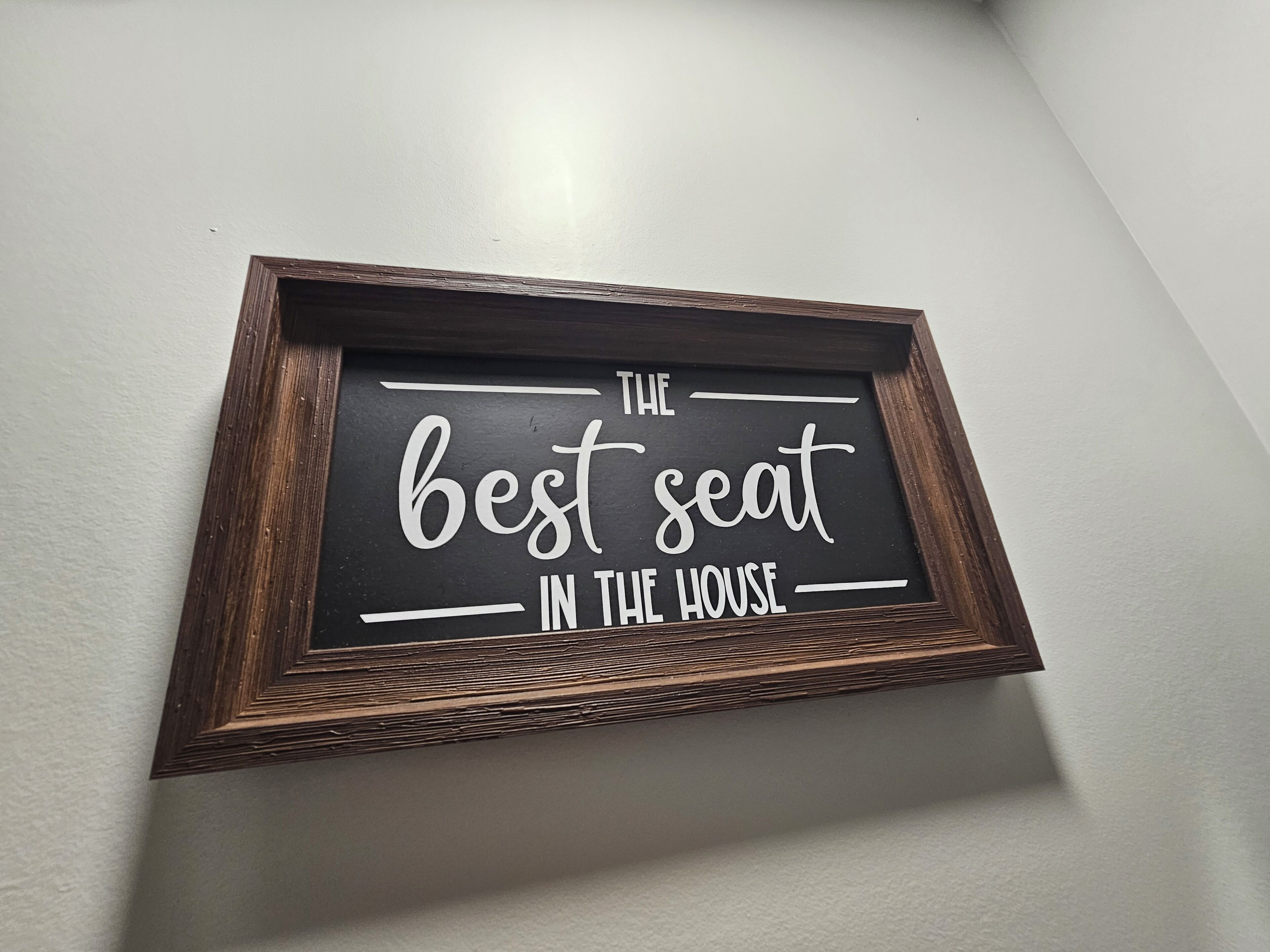 A framed sign with the text 'THE BEST SEAT IN THE HOUSE' on a wall.