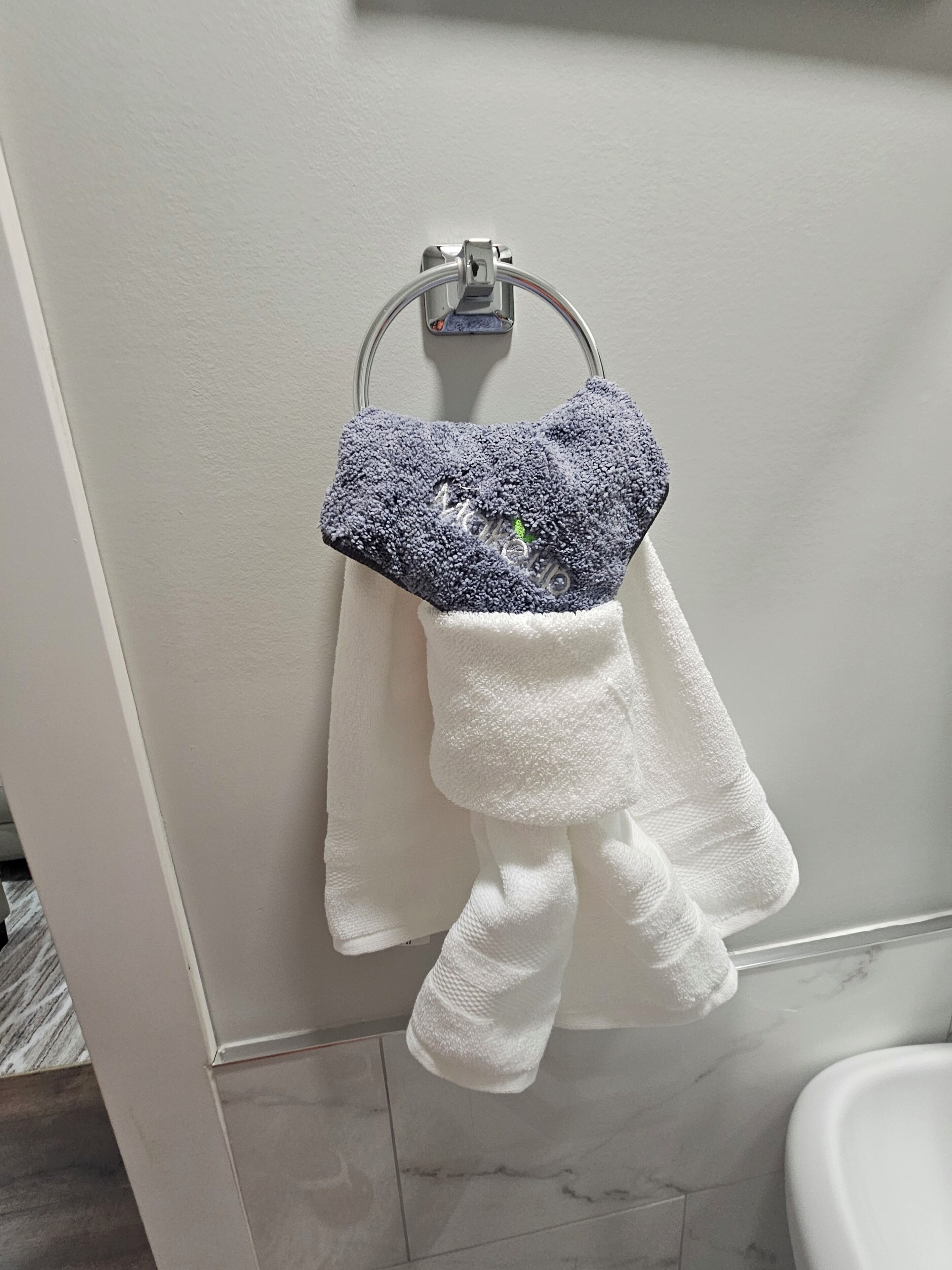 A bathroom with a white toilet, a white towel rack with a blue towel, and a white bath mat on the floor.