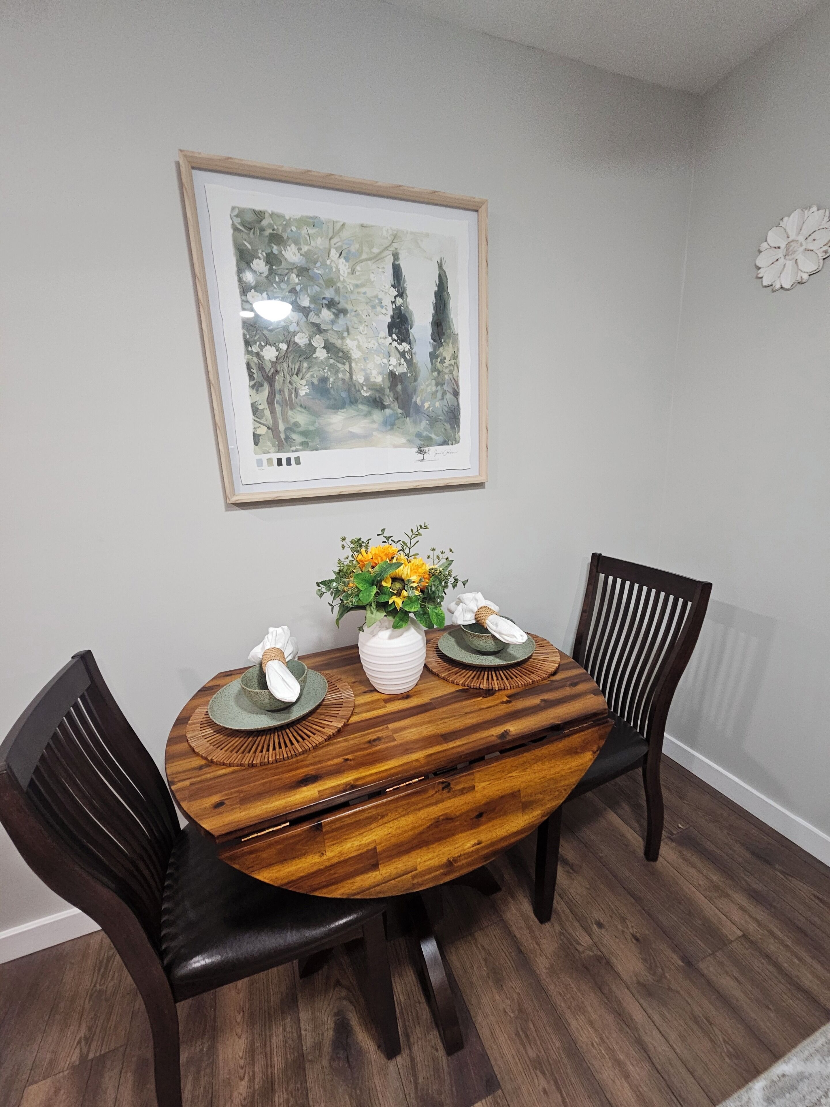 A dining table with a white vase, two green placemats, and a vase of yellow flowers.