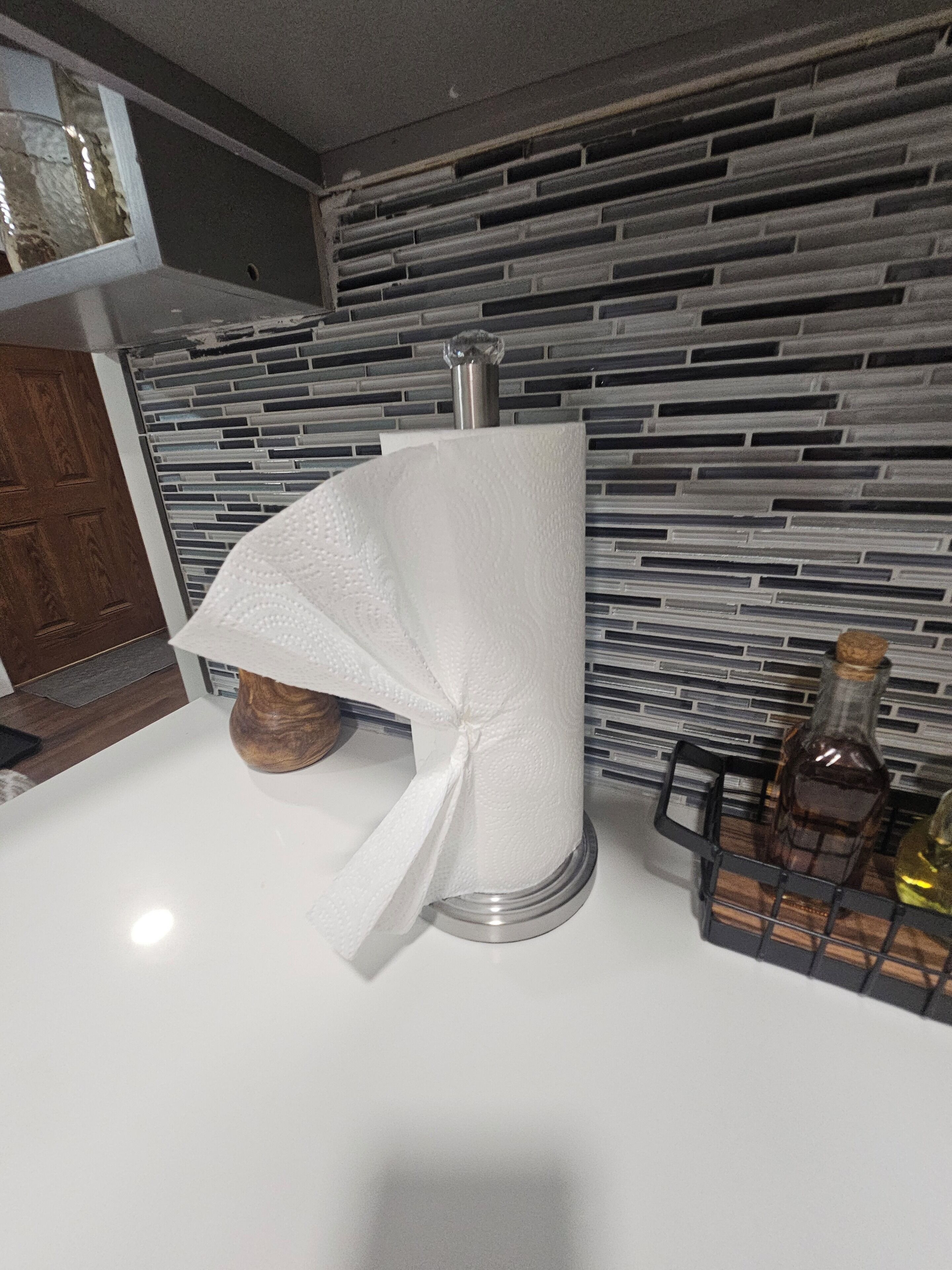 A kitchen with a modern design, featuring a roll of paper towels on a silver dispenser, a wooden bowl, and a bottle on the counter.