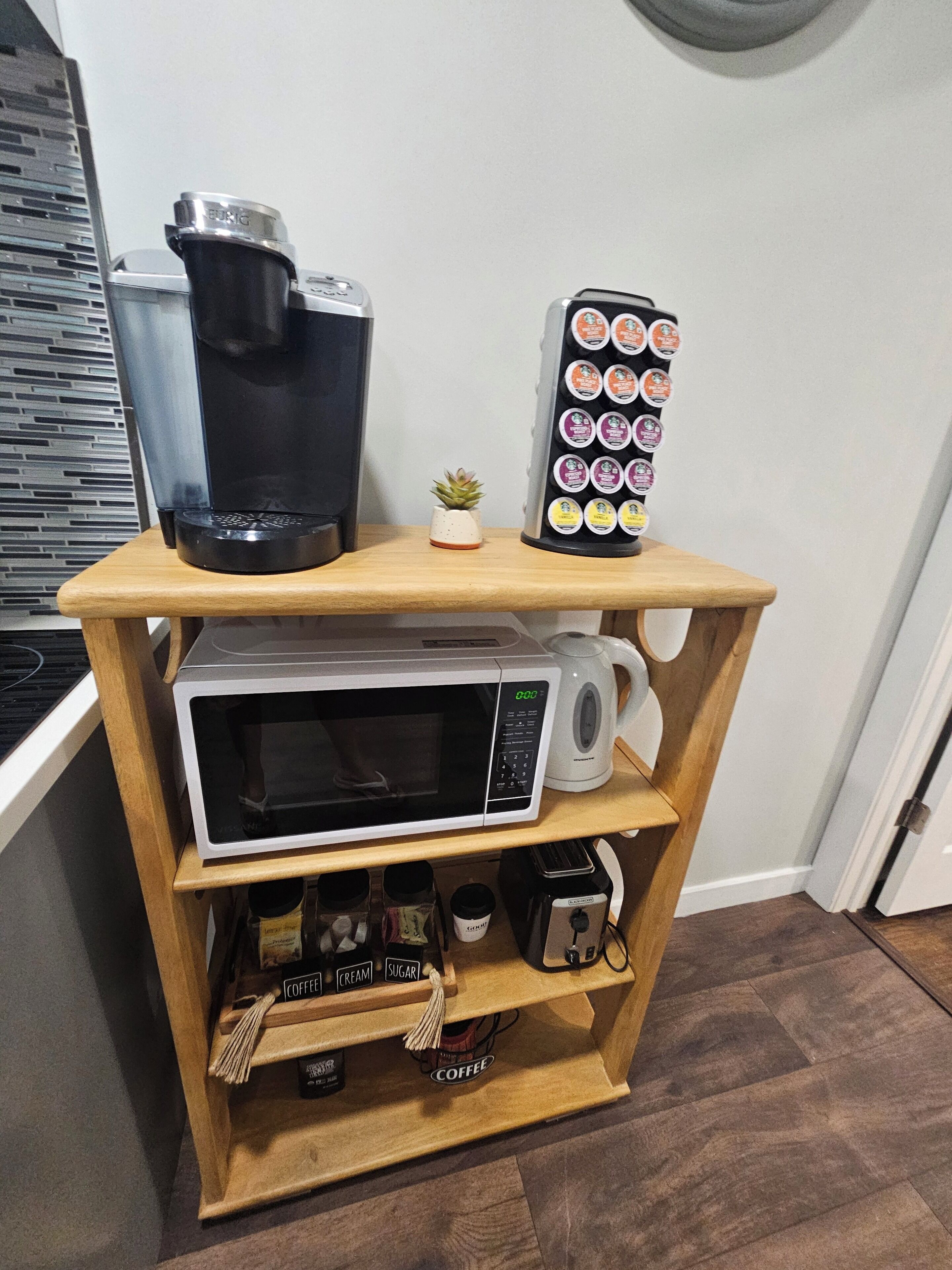 Una estantería de madera con una cafetera, un microondas y una pequeña planta en maceta.