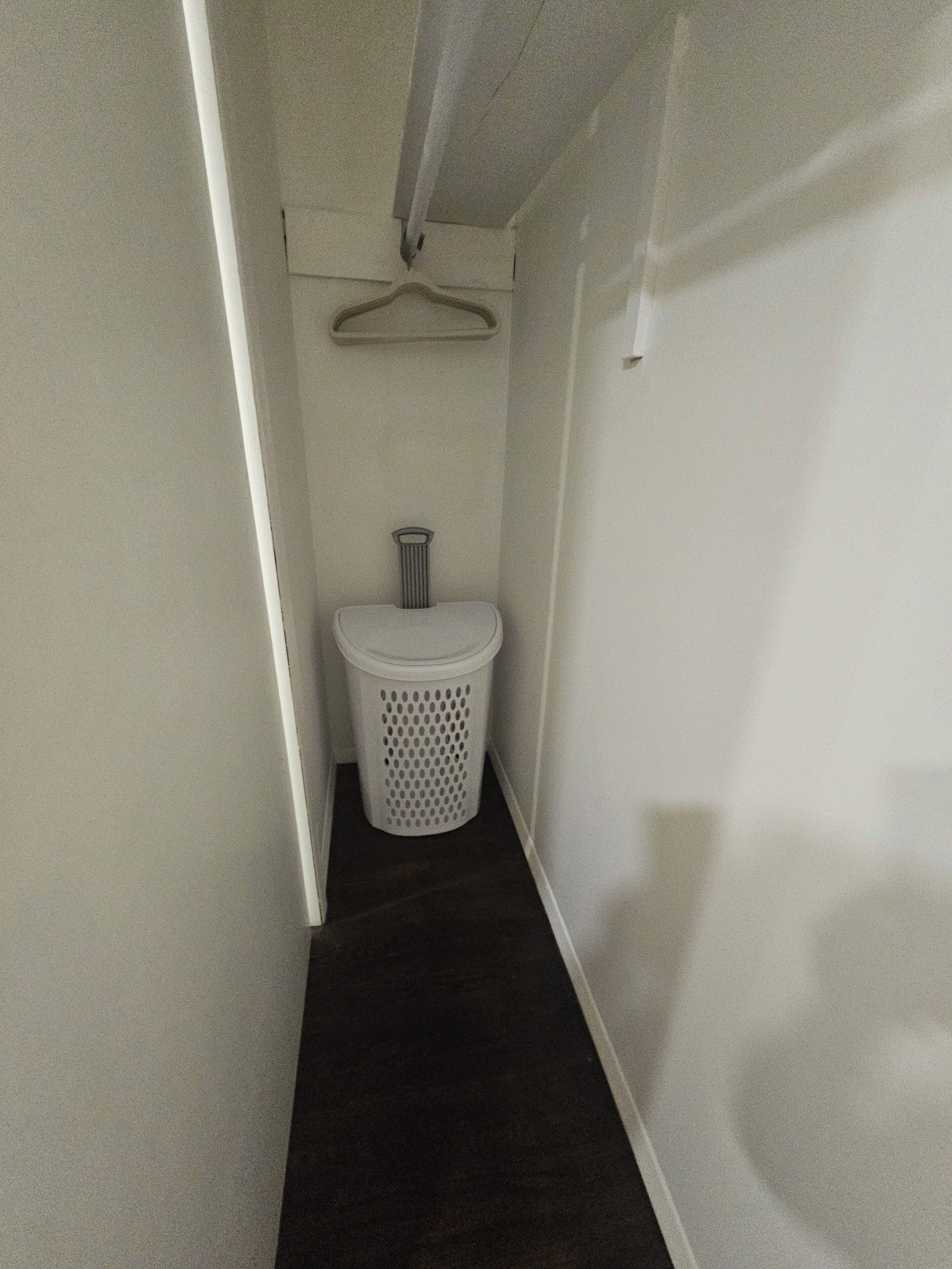 A narrow hallway with a white trash bin and a hanging laundry rack.