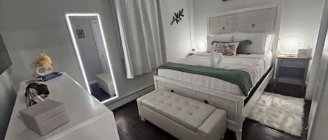 A bedroom with a bed, bedside tables, a mirror, a bench, and a wall sign.