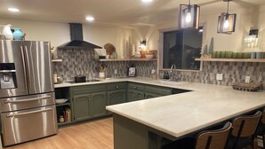 Een moderne keuken met een roestvrijstalen koelkast, een groot eiland met barstoelen en een betegelde spatwand.