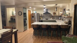 Een moderne keuken met een centraal eiland, barkrukken, een koelkast, oven en een klok aan de muur.