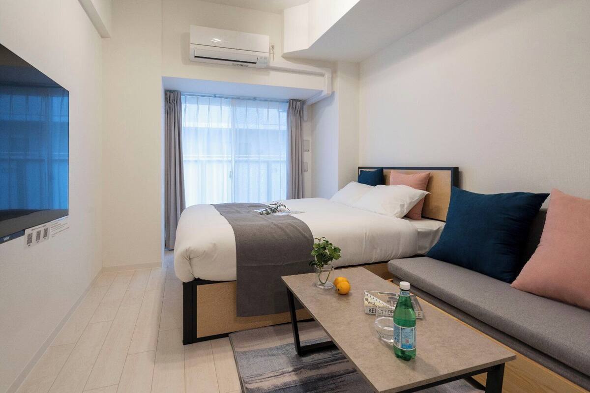 Una habitación de hotel moderna con una cama, un sofá, una mesita con una botella y un equipo de aire acondicionado.
