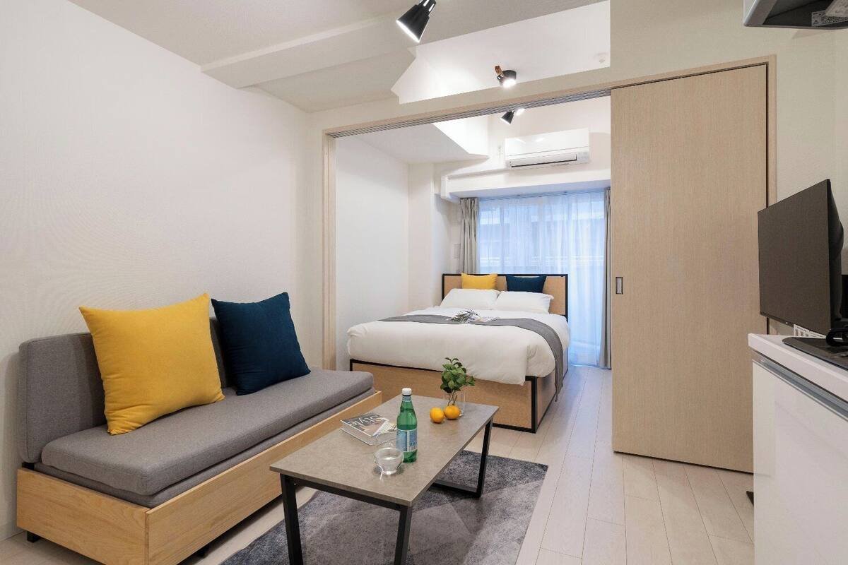 Una habitación de hotel moderna con un sofá, una cama, un televisor y una pequeña mesa con una botella y vasos.