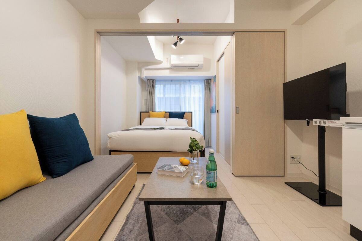 Una habitación de hotel moderna con sofá, cama, televisor y una mesita con planta y botella.