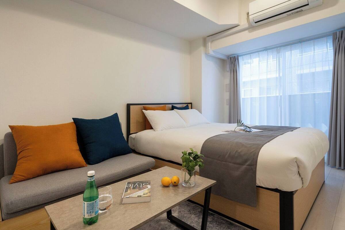Habitación de hotel con cama, sofá, mesa de centro con una revista, una botella y una planta.