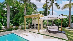 Un jardin avec une piscine, un espace salon couvert et un barbecue.