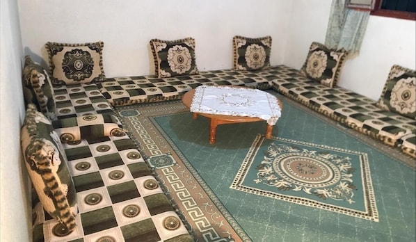 A room with a checkered floor, a central round table, and patterned cushions on a sofa.