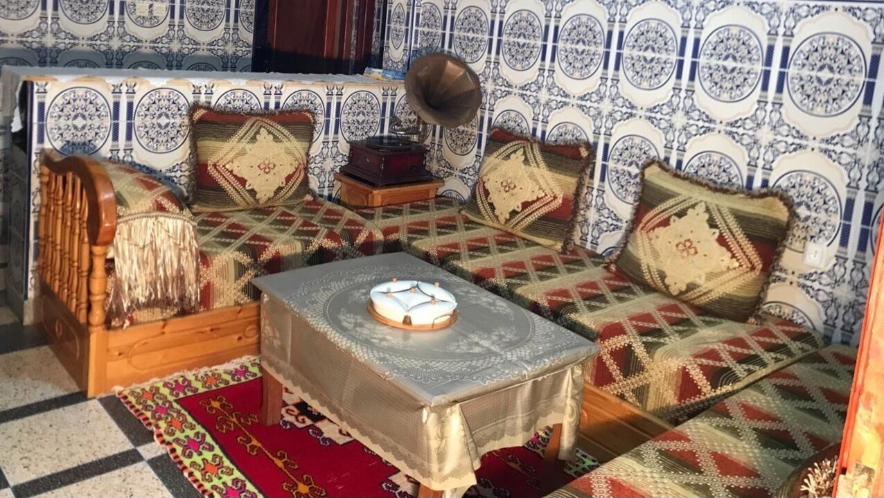 A traditional room with patterned walls, a sofa set, a table with a lace tablecloth, and a gramophone.