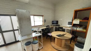 Una habitación con una mesa redonda de madera, un televisor, una computadora y una estantería con almohadas.