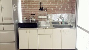 Una cocina con protector mural de ladrillo, un hervidor, un lavamanos y un refrigerador blanco.