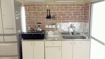 A kitchen with a brick backsplash, a kettle, a sink, and a white refrigerator.