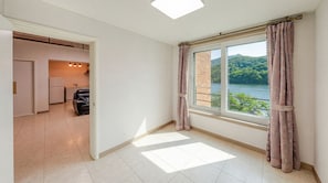 A room with a large window, a view of a lake, a kitchen area, and a seating area.